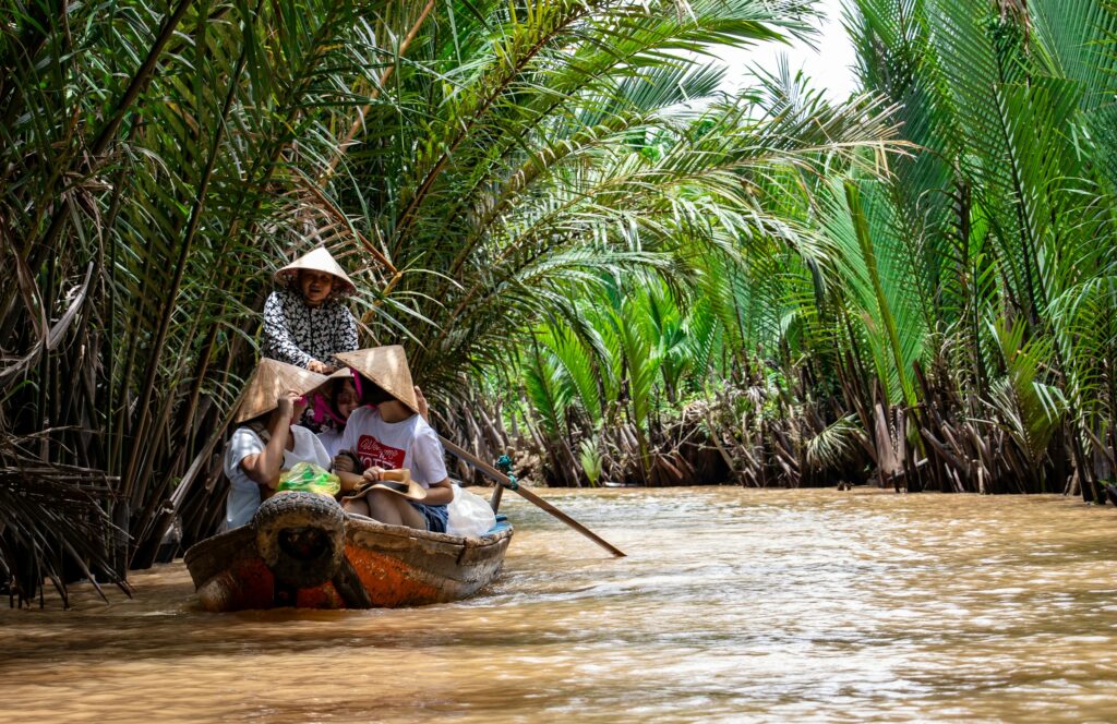 Travellers crossing a palm-lined canal by boat in the Mekong Delta